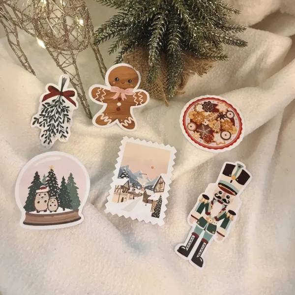 Un pack de six stickers de Noël comprenant un pain d'épice, un gui, des biscuits, une boule à neige, un village de noël et un casse noisette